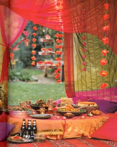 a table with food and drinks on it in front of an open window that has red drapes