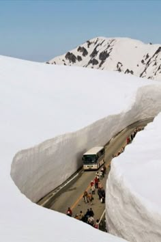 a bus driving down a snow covered road next to a large mountain filled with snow