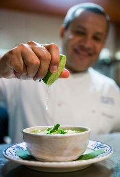 a man in a chef's uniform is holding a pickle over a bowl of soup