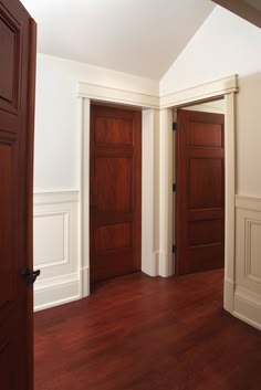 an empty room with wooden doors and hard wood flooring in the center, along with white walls