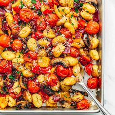 a pan filled with potatoes, tomatoes and other vegetables on top of a marble counter