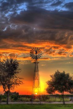 the sun is setting behind a windmill in an open field, with trees and grass