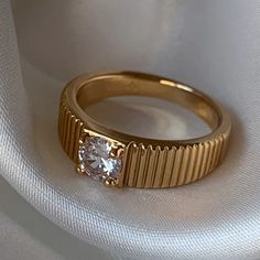 a gold ring with a white diamond on the top and bottom, sitting on a white cloth