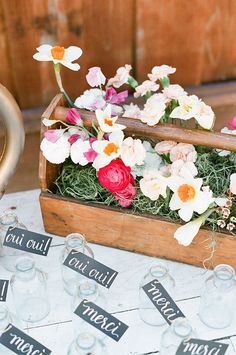 flowers are in a wooden box on a table with wine glasses and tags that say out call