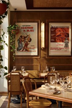 a restaurant with posters on the wall and wooden tables in front of them, along with empty wine glasses