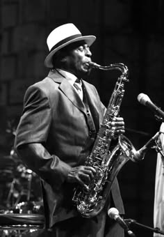 a man in a suit and hat playing a saxophone on stage with other musicians behind him