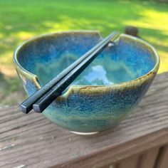 two chopsticks sticking out of a blue bowl on a wooden table outside with grass in the background