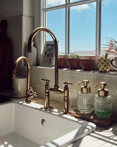 a kitchen sink with two faucets and soap dispensers in front of a window