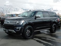 a black truck parked in a parking lot next to other cars and snow covered mountains