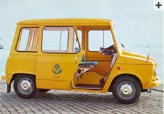 an old yellow van with the door open on a brick road next to a body of water