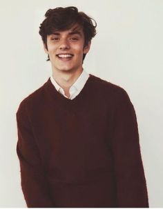 a young man wearing a brown sweater and white shirt