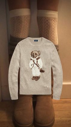 a sweater with a bear on it is hanging from the wall next to some brown boots