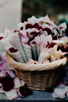 a wicker basket filled with pink and white flowers next to an open book on the ground