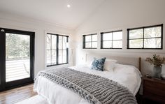 a large bed sitting next to two windows in a room with wooden floors and white walls