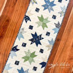 a quilted table runner with blue, green and white stars on the top is sitting on a wooden floor