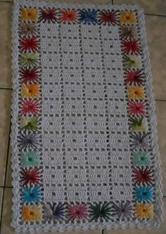 a white crocheted blanket with colorful flowers on the bottom and sides, sitting on a tile floor