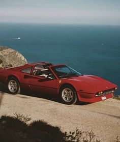 a red sports car parked on the side of a road next to the ocean in front of a cliff