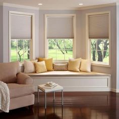 a window seat with pillows on it in front of two windows and a table next to it