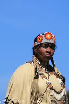 a native american woman wearing an elaborate headdress and feathers, standing in front of a blue sky