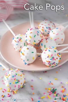 cake pops with white frosting and sprinkles on a pink plate