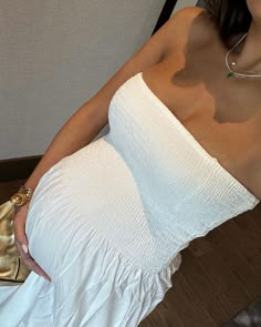 a woman in a white dress is holding a gold purse and posing for the camera