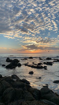 the sun is setting over the ocean and rocks