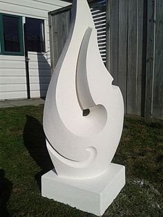 a large white sculpture sitting on top of a lush green field next to a building