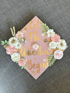 a pink graduation cap with flowers and let the adventure begin written on it in gold lettering