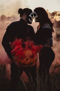 two people with painted faces standing next to each other holding a pumpkin in their hands