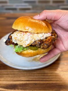 a hand holding a chicken sandwich over a white plate