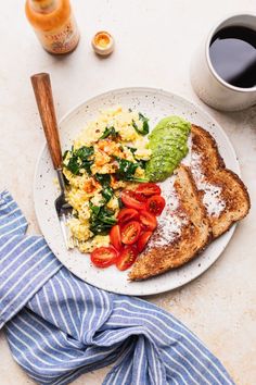 greek yogurt scrambled eggs with tomatoes and spinach on a plate next to a cup of coffee