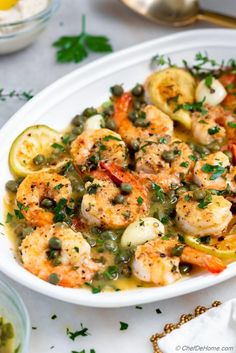 a white bowl filled with shrimp and vegetables on top of a table next to silverware