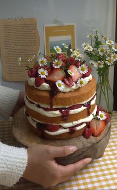 a cake with strawberries and daisies on top is displayed in front of the camera