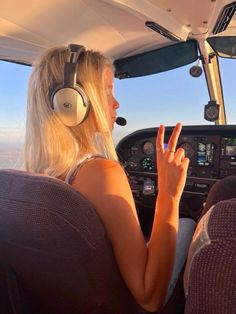 a woman sitting in the cockpit of an airplane with headphones on and pointing at something