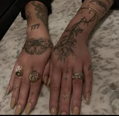 two hands with tattoos and rings on them sitting on a counter top next to each other