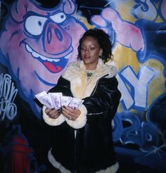 a woman standing in front of a wall with graffiti on it and holding cash bills