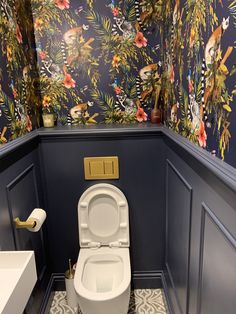 a toilet in a bathroom with blue walls and floral wallpapers on the walls