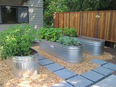 three metal planters filled with plants in front of a house