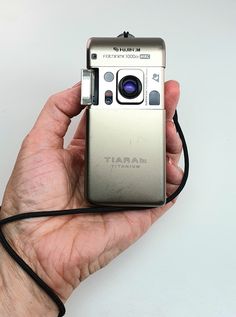 a hand holding a silver camera with a black cord in it's left hand