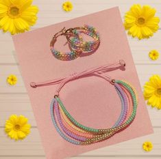 three bracelets and two rings on top of a pink paper with yellow flowers in the background