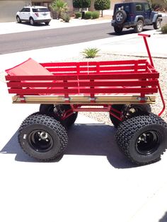 a red wagon with four wheels parked on the side of a road in front of a house