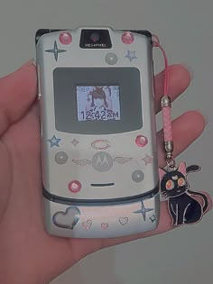 a person holding a cell phone with a cat keychain attached to the back