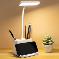 a desk lamp that is next to a pot with pens and pencils in it