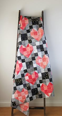 a patchwork heart quilt hanging on a wooden chair in front of a white wall