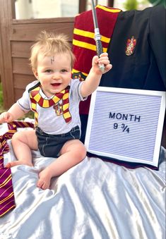 a baby sitting on top of a bed next to a harry potter costume and wand