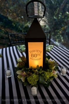 a lantern is lit on top of a table with flowers and greenery around it