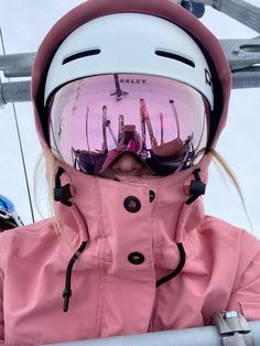 a girl wearing ski goggles and a pink coat on the side of a ski lift