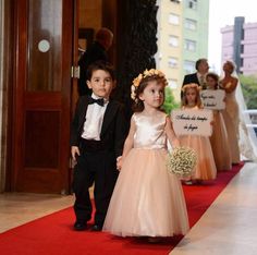 two young children in formal wear walking down the red carpeted aisle at a wedding