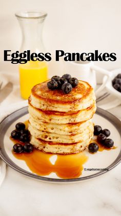 a stack of pancakes with blueberries and syrup on a plate next to a glass of orange juice