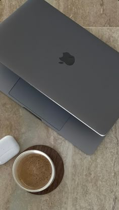 an apple laptop sitting on top of a table next to a cup of coffee